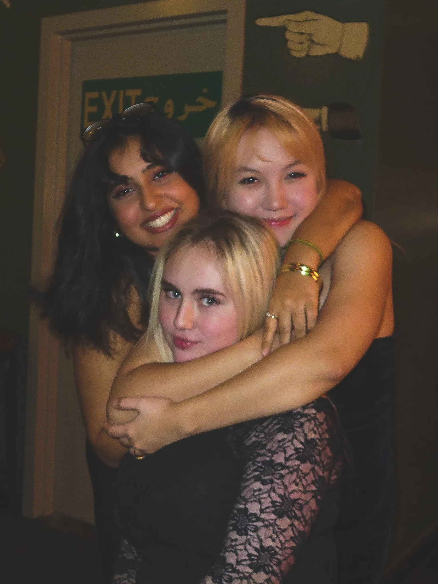 Three friends hugging and posing together beside an exit sign